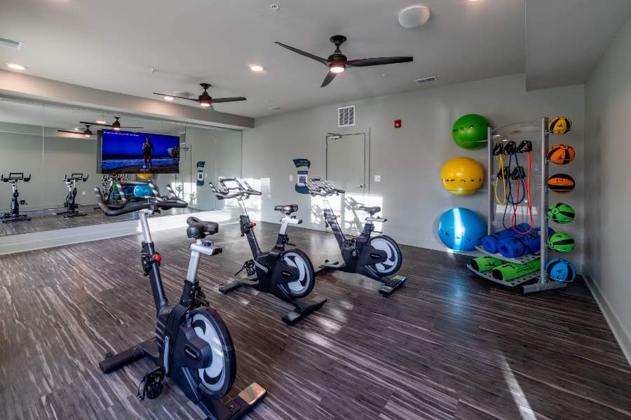 Apartment fitness center with a mirrored wall, exercise bikes, and stability balls.